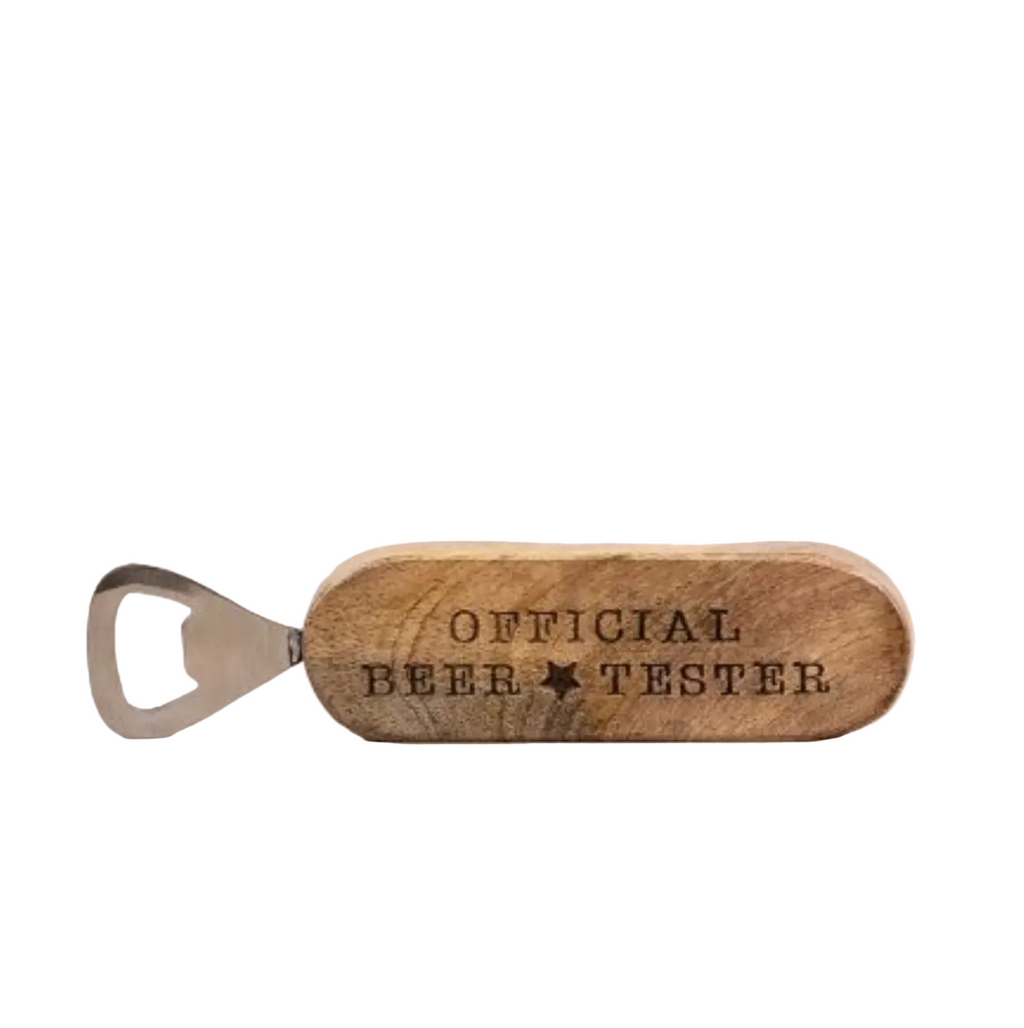 A wooden bottle opener engraved with 'OFFICIAL BEER TESTER' and a star, resting on a light wood surface against a white background.