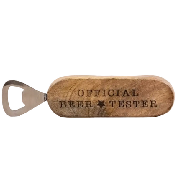 A wooden bottle opener engraved with 'OFFICIAL BEER TESTER' and a star, resting on a light wood surface against a white background.