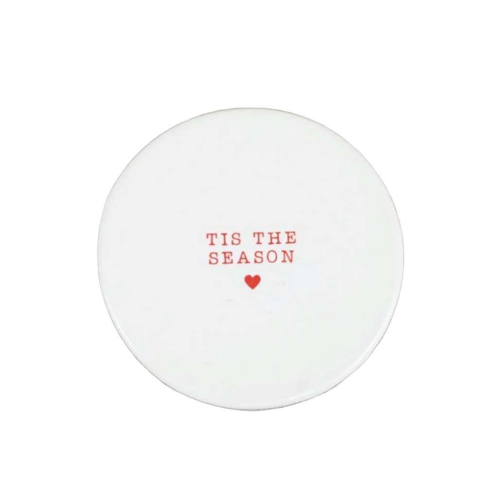 A round white ceramic coaster with the phrase 'TIS THE SEASON' and a small red heart printed in the center.