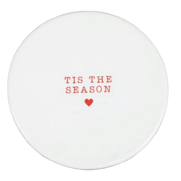 A round white ceramic coaster with the phrase 'TIS THE SEASON' and a small red heart printed in the center.