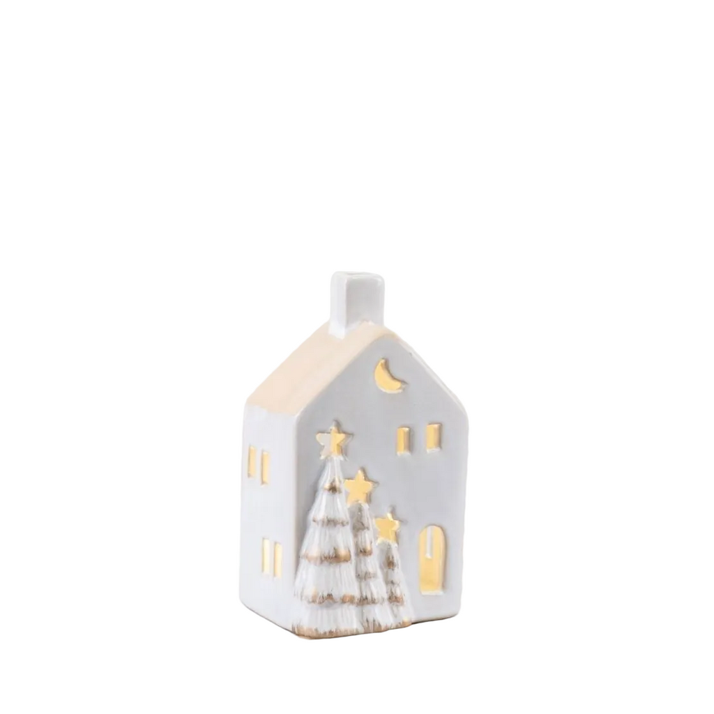 A small white ceramic house-shaped candle holder with gold-toned cutout details, including a crescent moon, stars, and two Christmas trees, against a white background.