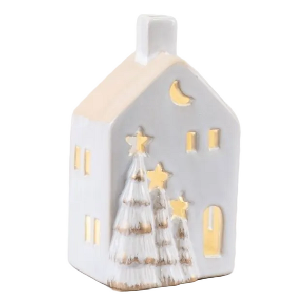 A small white ceramic house-shaped candle holder with gold-toned cutout details, including a crescent moon, stars, and two Christmas trees, against a white background.
