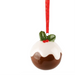 A Christmas pudding ornament shaped like a glossy brown pudding with white icing, a green holly leaf, and red berries, hanging from a red ribbon on a white background.