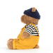 Teddy bear wearing a navy hat, striped shirt, and yellow apron on a white background