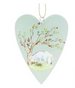 A heart-shaped ceramic ornament featuring a painted illustration of a white pig standing under a tree with red berries, suspended by a gold string on a white background.