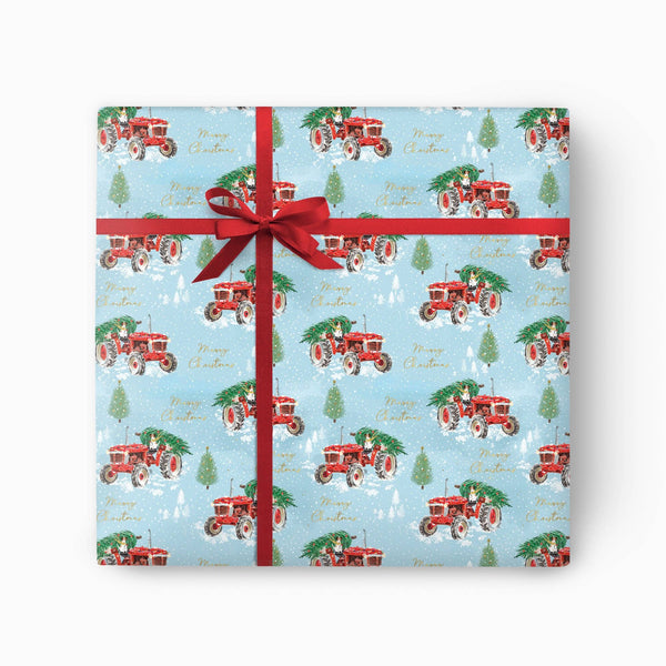A square gift box wrapped in light blue Christmas-themed wrapping paper with a red tractor and tree pattern, tied with a red ribbon and bow on a white background.