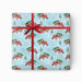 A square gift box wrapped in light blue Christmas-themed wrapping paper with a red tractor and tree pattern, tied with a red ribbon and bow on a white background.