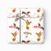 A square gift box wrapped in white Christmas-themed paper with a pattern of dachshunds in red sweaters, green boots, red and pink presents, gold stars, and 'MERRY CHRISTMAS' text, tied with a gray ribbon and bow.