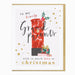 A square greeting card with a white background and a thin gold border, featuring a festive illustration of a red patterned jar filled with ornaments and a small gift box, with the text 'to my lovely Grand parents with so much love at Christmas'.