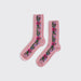 A pair of light pink crew socks with a vertical floral pattern in pink, purple, and green, featuring a decorative lace-like trim along the sides, shown on a light gray background.