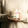 Person holding a candle with 'AGNES + CAT' branding in a warm setting.