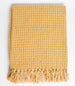 Yellow woven blanket with tassels on a light gray background