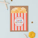 Mrs Best Paper Co. popcorn-shaped birthday card with red and white stripes and a kraft envelope on a desk.