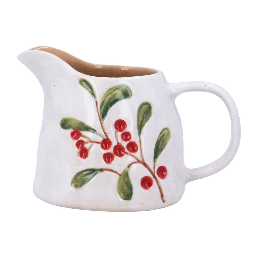 A white ceramic milk pitcher decorated with a hand-painted green mistletoe branch with red berries, shown against a plain white background.