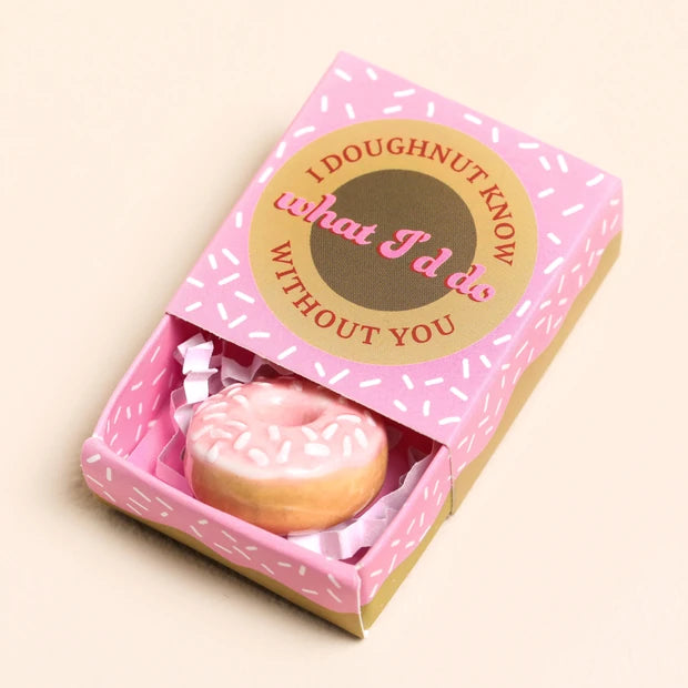 Pink donut-shaped token in a decorative box with text on a beige background