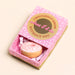 Pink donut-shaped token in a decorative box with text on a beige background