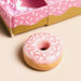 Pink frosted donut with sprinkles on a beige surface
